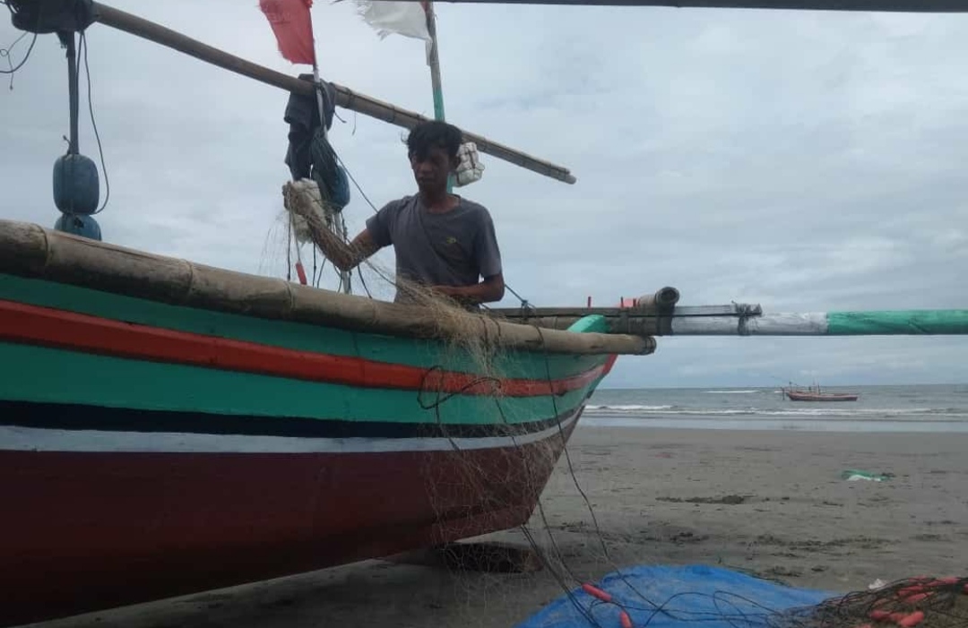 Nelayan Malabero yang tidak melaut sembari memperbaiki jaring yang dipakai untuk melaut.